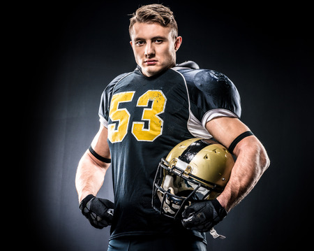 American football player holding helmet and looking at camera on blackの写真素材