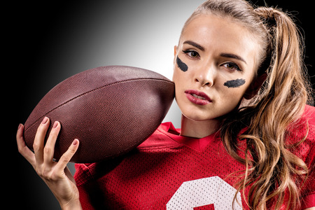 Close-up portrait of female american football player holding ball and looking at camera on blackの写真素材