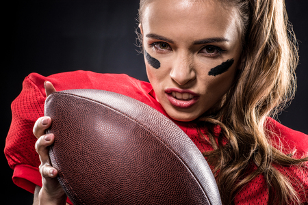 Close-up portrait of female american football player holding ball and looking at camera on blackの写真素材