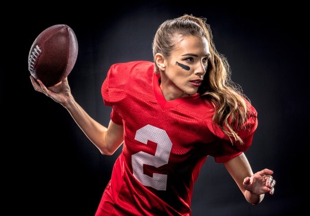 Beautiful woman in uniform playing american football with ball on blackの写真素材