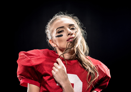 Close-up portrait of attractive female american football player in uniform posing on blackの写真素材