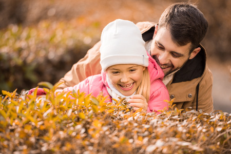 Close-up portrait of adorable little girl playing with smiling father in autumn parkの写真素材