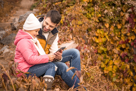 Happy father with daughter sitting outdoors and using tablet computer