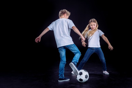 Happy brother and sister playing with soccer ball on blackの写真素材