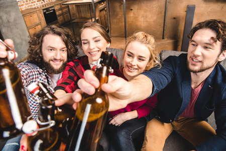 Smiling friends holding beer bottles while sitting on sofaの写真素材