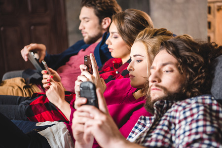 Side view of serious friends using digital devices at homeの写真素材
