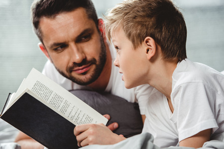 Close-up portrait of father and son reading book in bedの写真素材