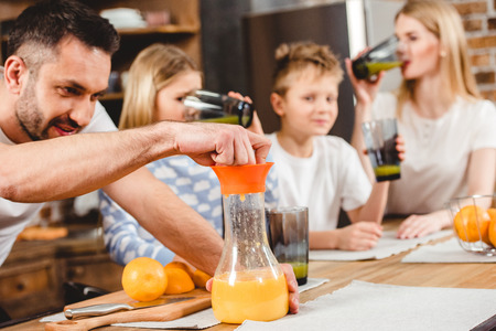 Young man makes orange juice for his family for breakfastの写真素材