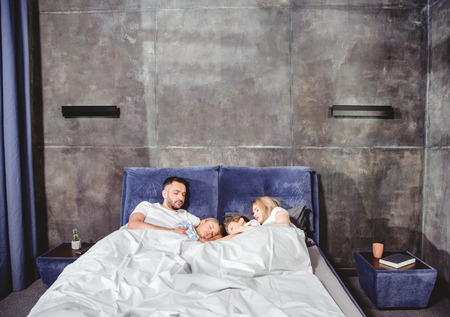 Happy family lying in bed under white duvet in cozy bedroomの写真素材