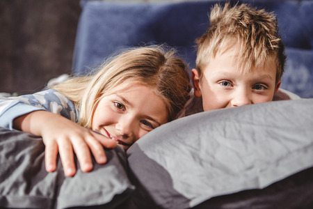 Cute smiling brother and sister lying on grey pillows and looking at cameraの写真素材