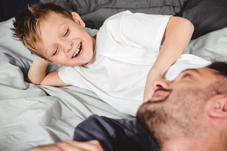 Happy father and his little son lying on bed and looking at each otherの写真素材