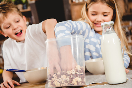 Brother and sister have corn flake rings for breakfast sitting at the table in kitchenの写真素材
