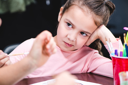 Close-up portrait of bored schoolchild sitting at table and looking awayの写真素材