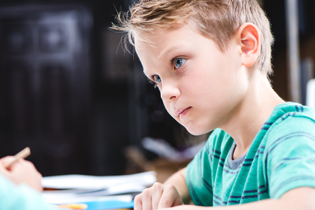 Close-up portrait of concentrated schoolchild sitting at table and studyingの写真素材