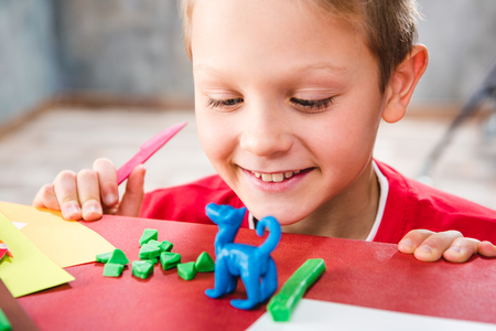 Close-up portrait of smiling schoolchild making toy from plasticineの写真素材