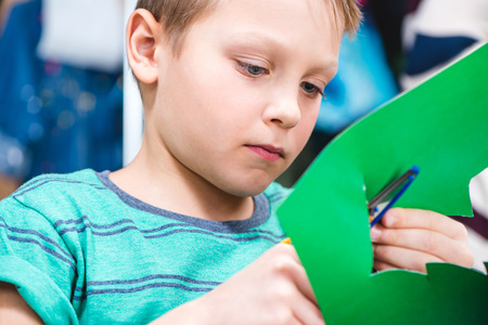 Close-up portrait of schoolchild cutting green paper with scissorsの写真素材