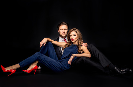Portrait of beautiful sensual couple in elegant clothes lying and looking at camera on blackの写真素材