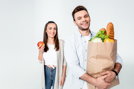 woman with apple looking at smiling man holding grocery bagの写真素材