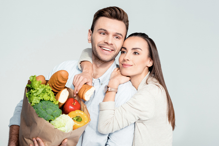 happy woman hugging man with grocery bag and looking awayの写真素材