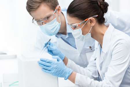 man and woman scientists in protective glasses and masks making experimentの写真素材
