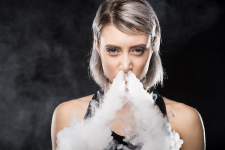 woman vaping and blowing smoke of electronic cigarette from noseの写真素材