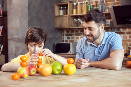 father and son playing with citrus fruits at kitchen tableの写真素材