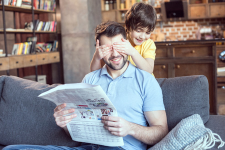boy closing fathers eyes while reading newspaperの写真素材