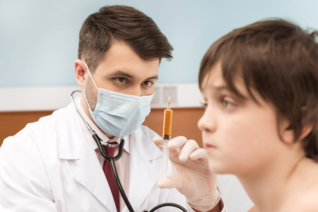 doctor in medical mask holding syringe for injection to boy patientの写真素材