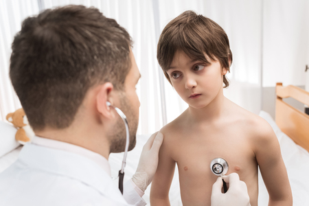 doctor examining little boy with stethoscope in hospitalの写真素材