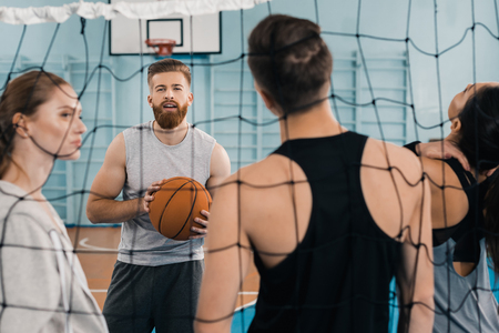 young sportsman with ball talking with teammates in sports hallの写真素材
