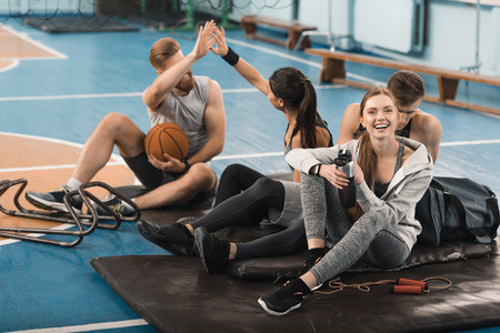 young sporty people sitting on mats and talking in sports hallの写真素材