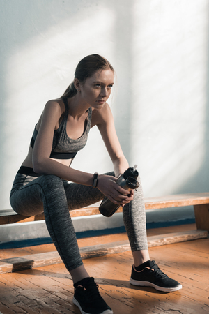 sporty woman sitting on bench with bottle of waterの写真素材