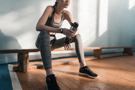 sporty woman sitting on bench with bottle of waterの写真素材