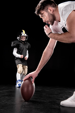 Trainer holding rugby ball and boy preparing to play american footballの写真素材