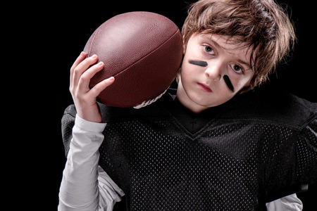 boy american football player holding rugby ball and looking at cameraの写真素材