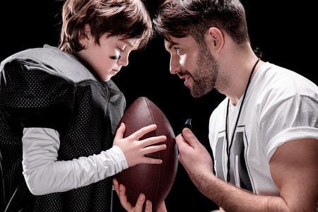 trainer and boy with rugby ball standing face to face on blackの写真素材