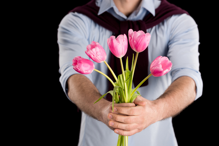 Close-up partial view of man presenting beautiful pink tulips on blackの写真素材