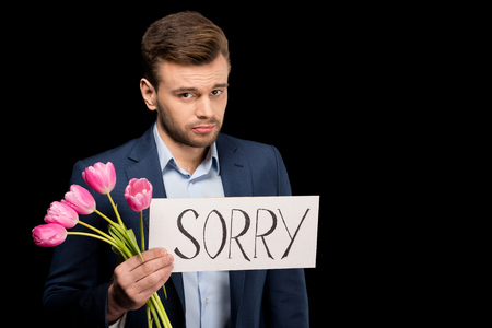 young man with tulips and sorry sign looking at cameraの写真素材
