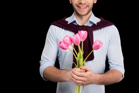 Cropped shot of smiling young man holding pink tulips on blackの写真素材