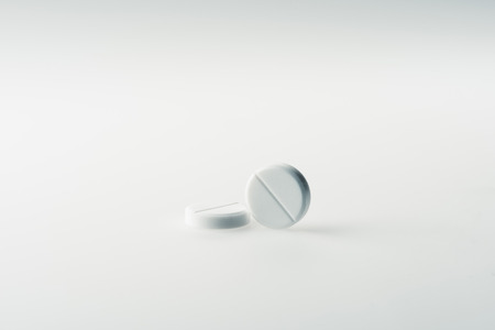 Two round white medical tablets on grey background