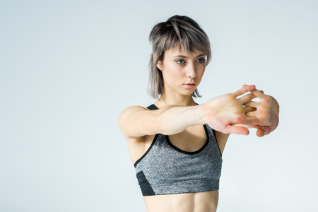 young woman in sportswear stretching arms on grey