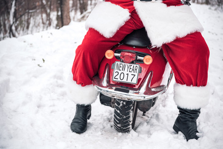 Low section of Santa Claus sitting on red motorbike with plat New Year 2017 sign on snowy trailの写真素材
