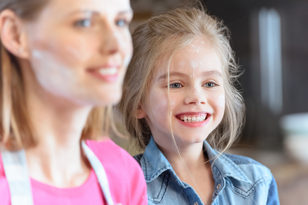 cheerful mother and daughter in flour in kitchenの写真素材