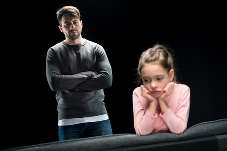 father with crossed arms looking at upset little daughter, family problems conceptの写真素材
