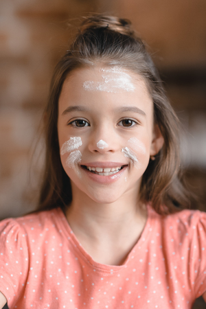little girl with flour on face smiling at cameraの写真素材