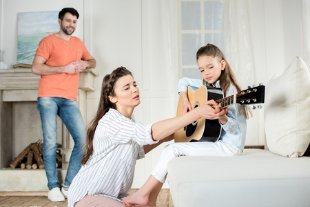father looking at mother with daughter playing guitar at homeの写真素材