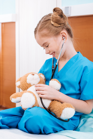 smiling girl nurse listening teddy bears heartbeat with stethoscopeの写真素材