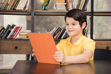 schoolboy sitting at table and using digital tablet