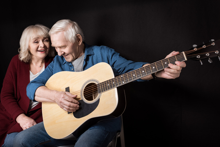 side view of senior man playing guitar with wife near byの写真素材