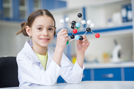 Girl scientist in lab coat holding molecular model and smilingの写真素材
